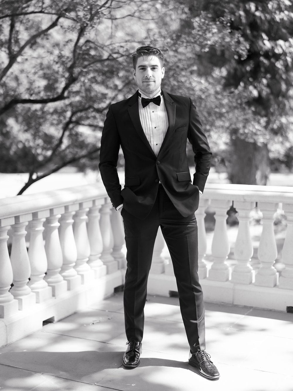 groom stands with hands in pocket of black tux on patio at the Ashford Estate