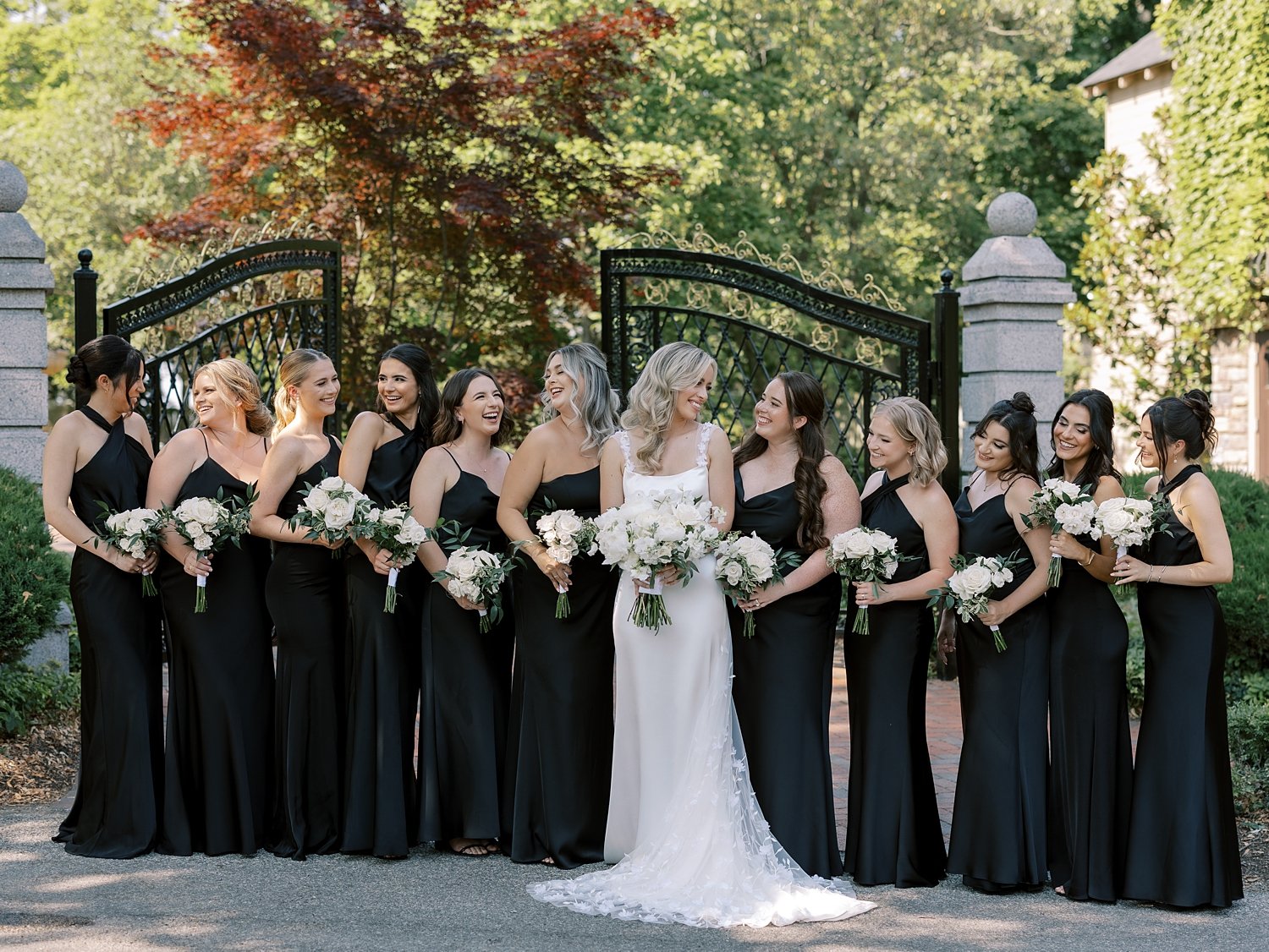 bride and bridesmaids in mismatched black dresses pose outside black gate at the Ashford Estate
