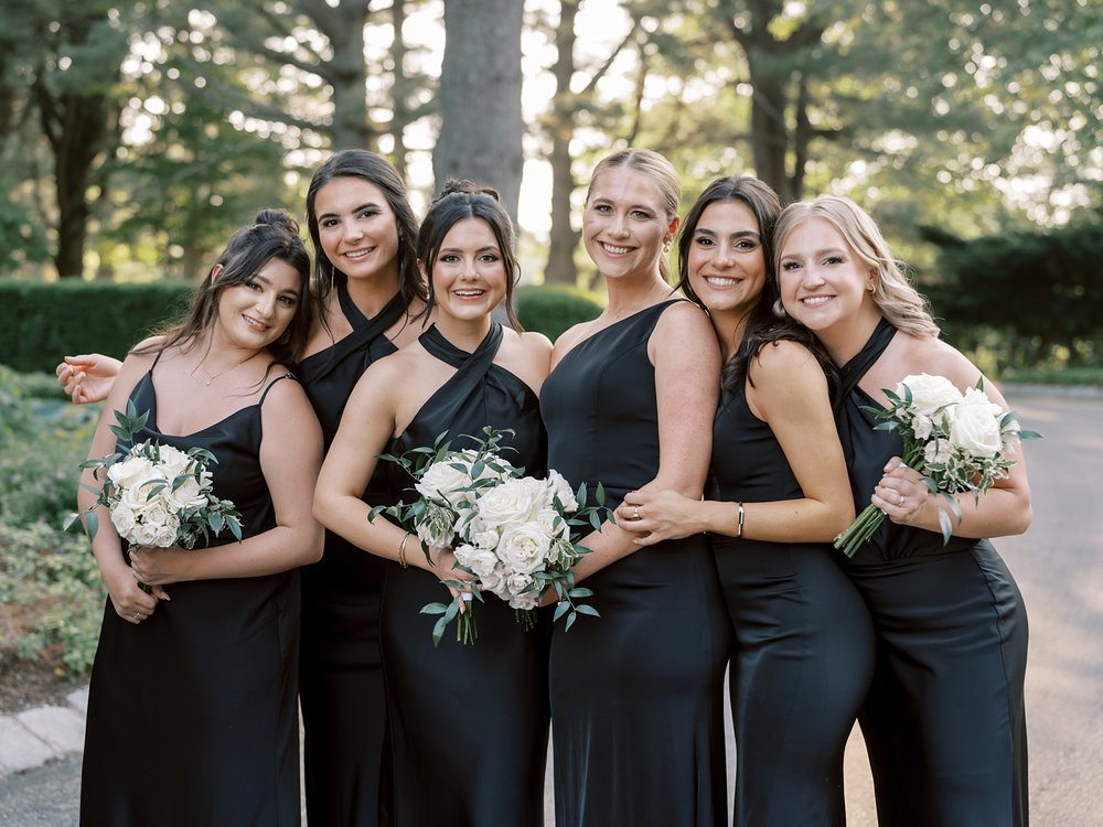 bridesmaids hug together in black dresses with white bouquets 