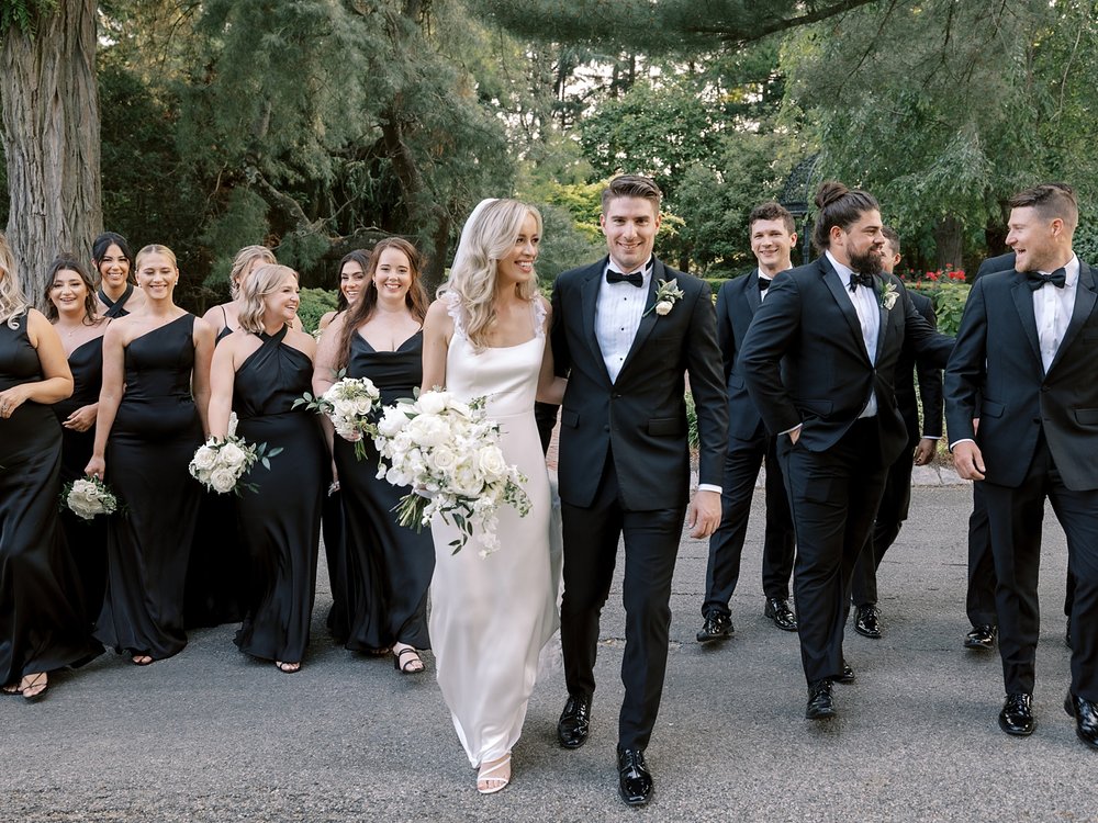 bride and groom hug walking on driveway with bridal party behind them 