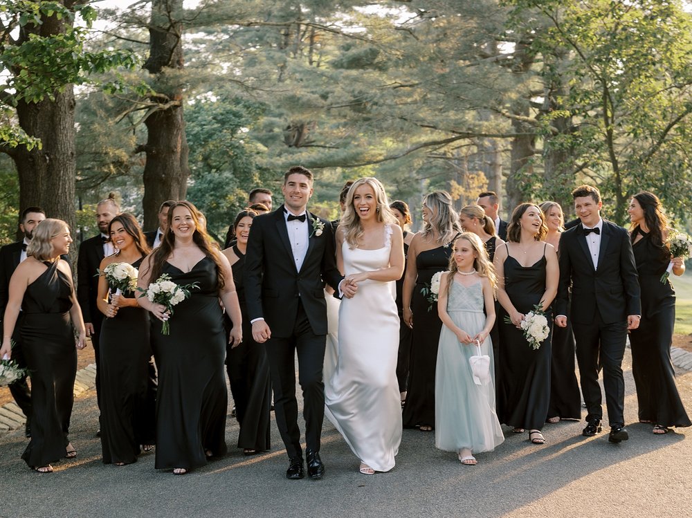bride and groom walk with wedding party in black and white attire