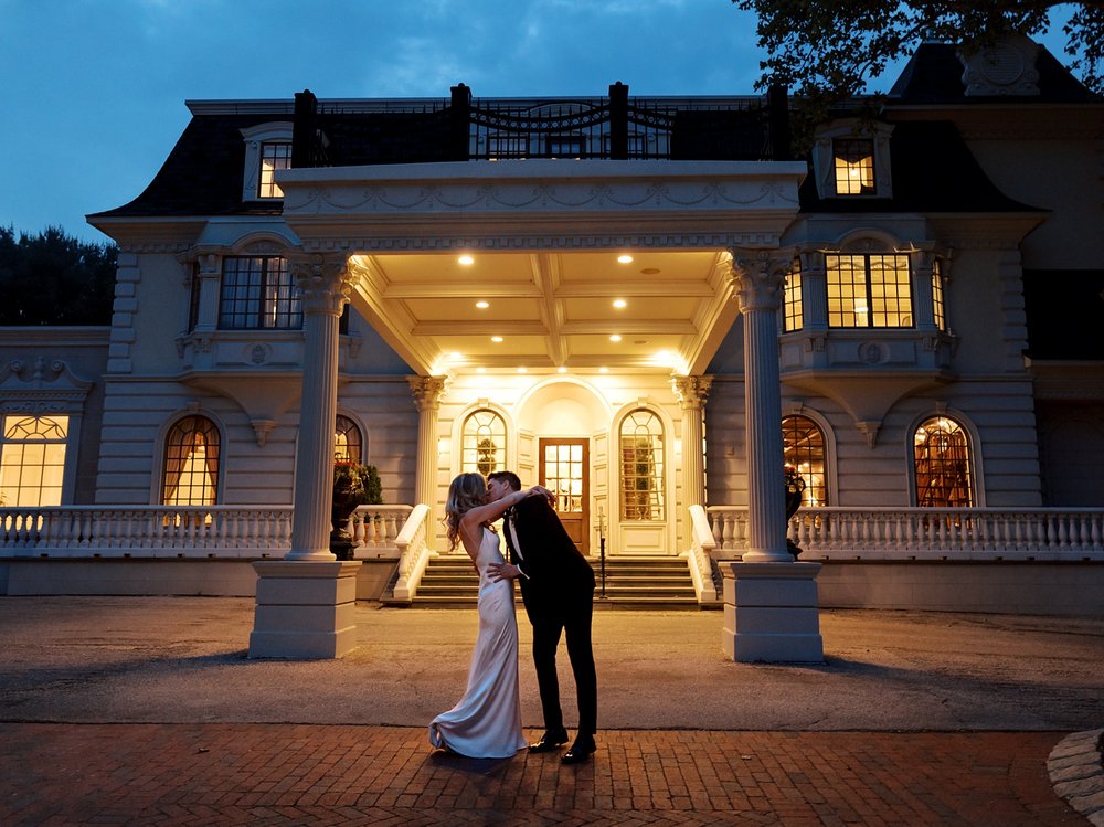 newlyweds kiss leaning together outside the Ashford Estate at night