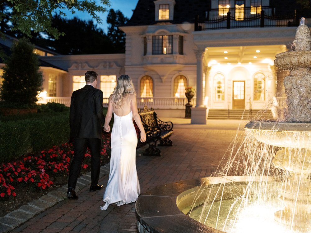 newlyweds walk outside the Ashford Estate at night with fountain lit up