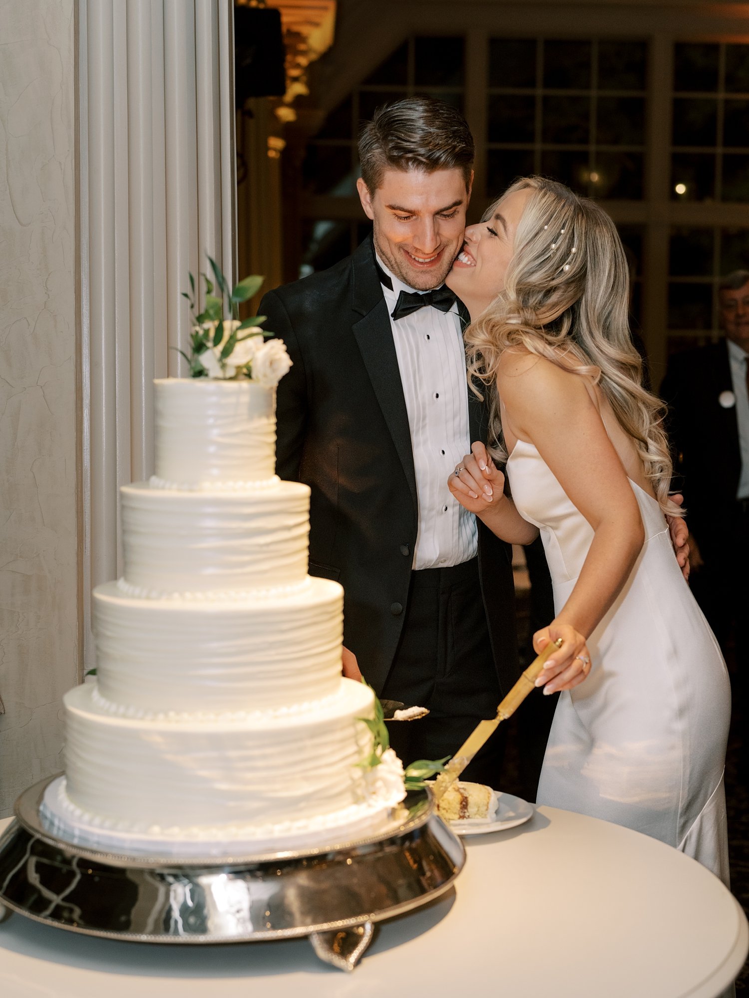 newlyweds kiss by tiered wedding cake at the Ashford Estate