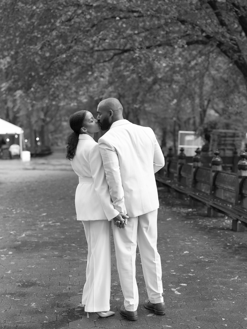 man and wife kiss in pathway of Central Park during rainy anniversary session
