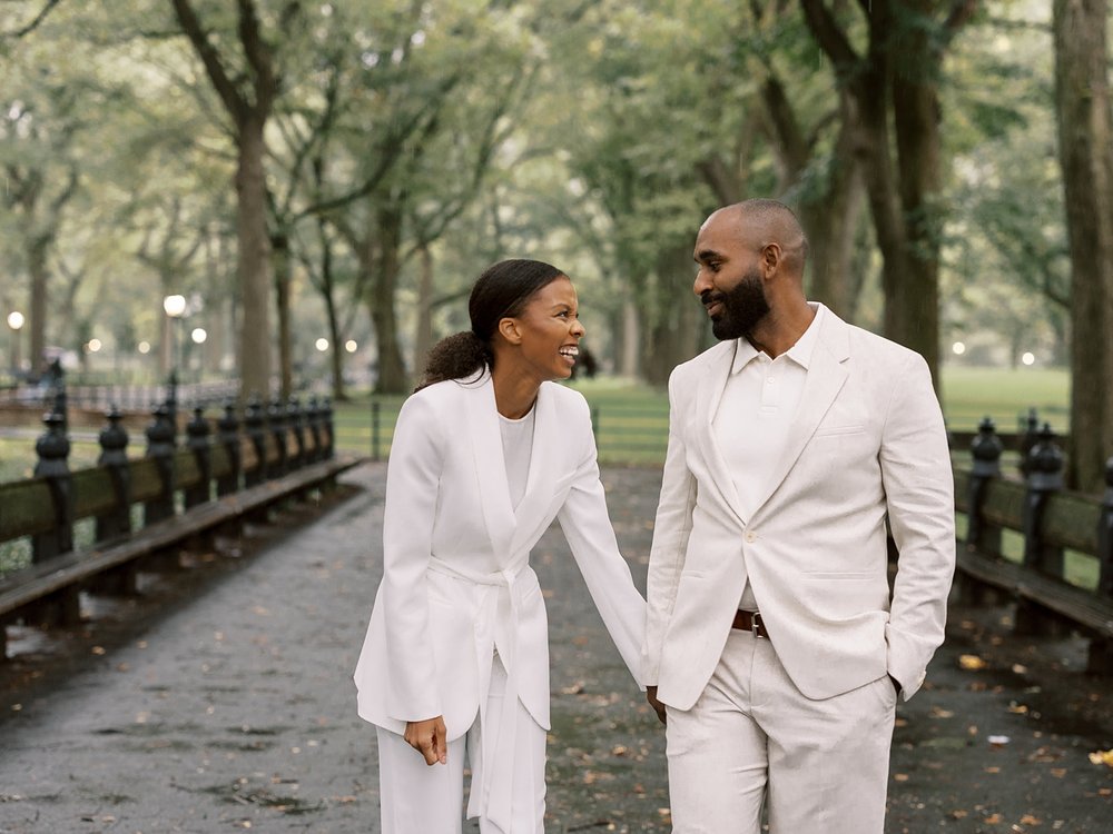 married couple holds hands laughing while they walk through Central Park