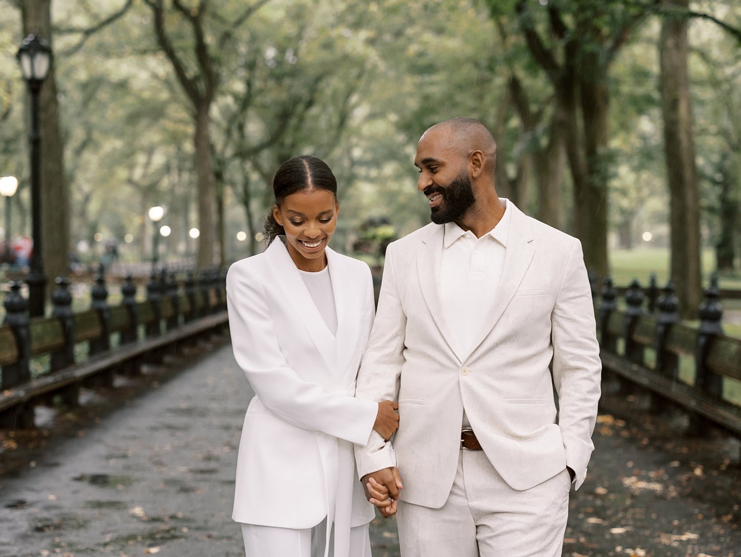 married couple holds hands laughing and walking through Central Park