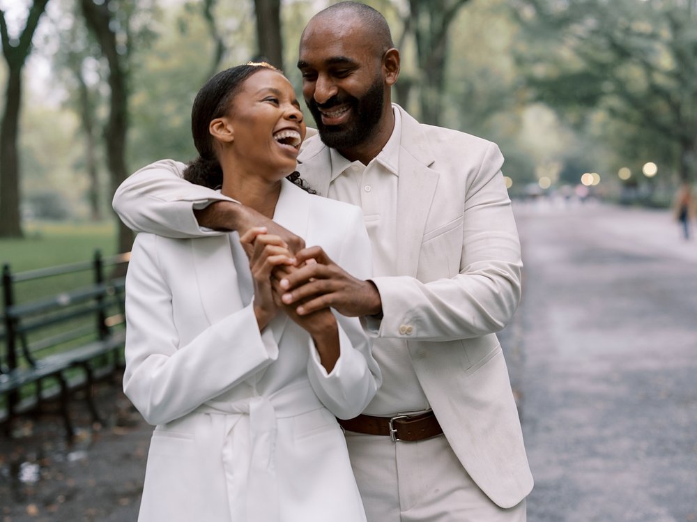 man hugs wife from behind marking her laugh in Central Park