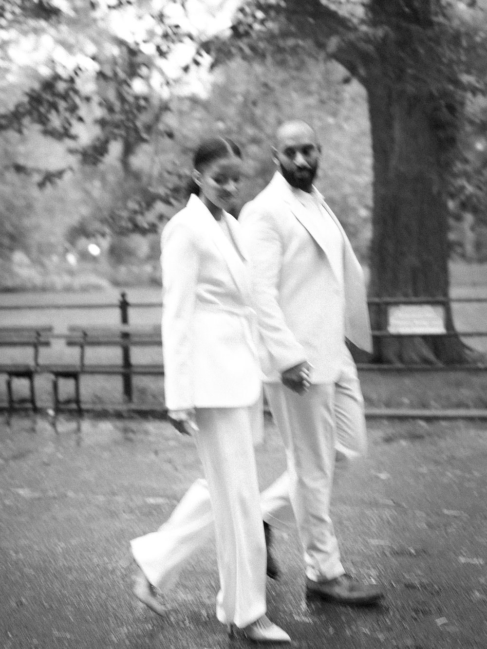 husband and wife hold hands walking through Central Park in the rain