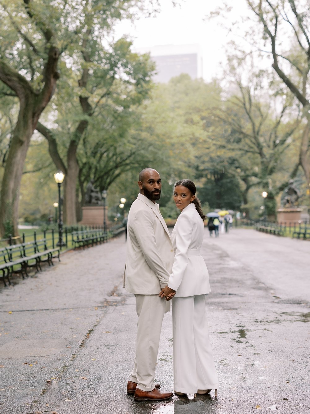 husband and wife hold hands turning to camera at Central Park