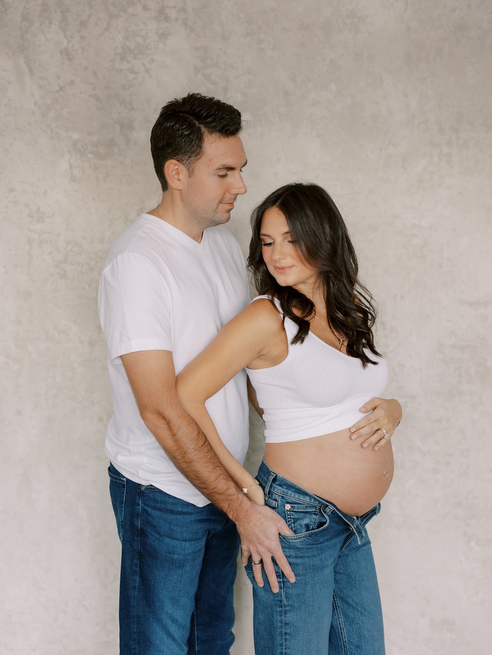 man hugs wife to him holding hip in jeans doing studio maternity portraits in New York City