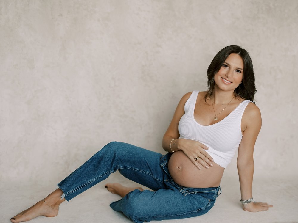 woman sits holding baby bump during studio maternity portraits in New York City