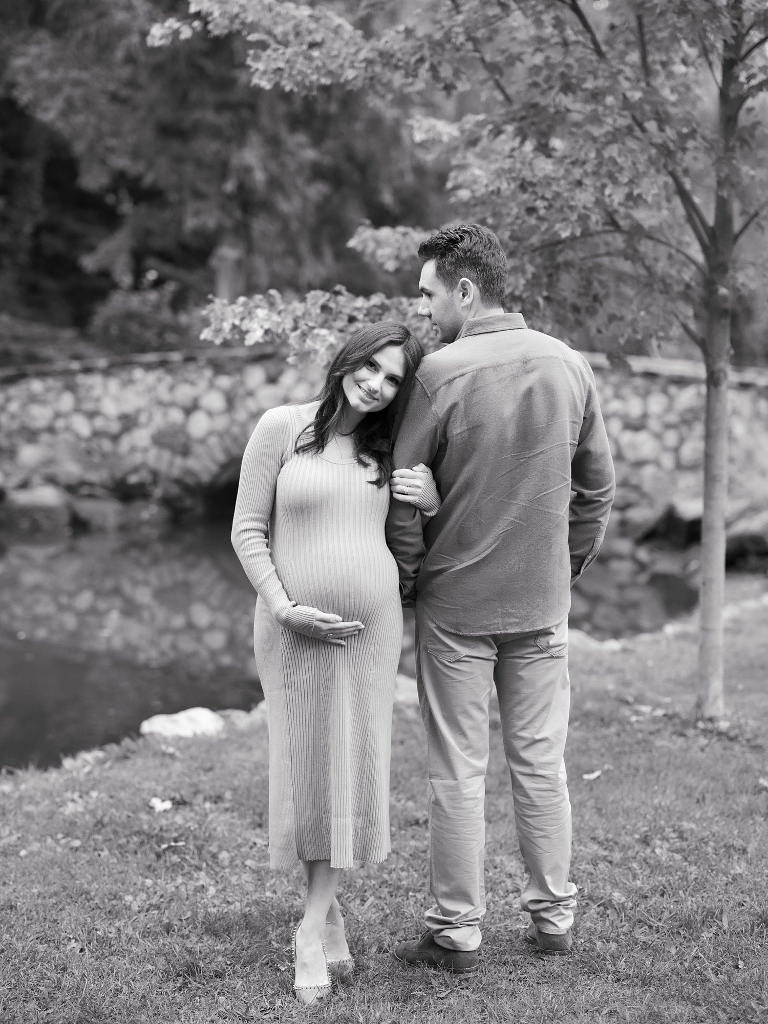 woman leans on husband's shoulder while cradling baby bump in NYC park