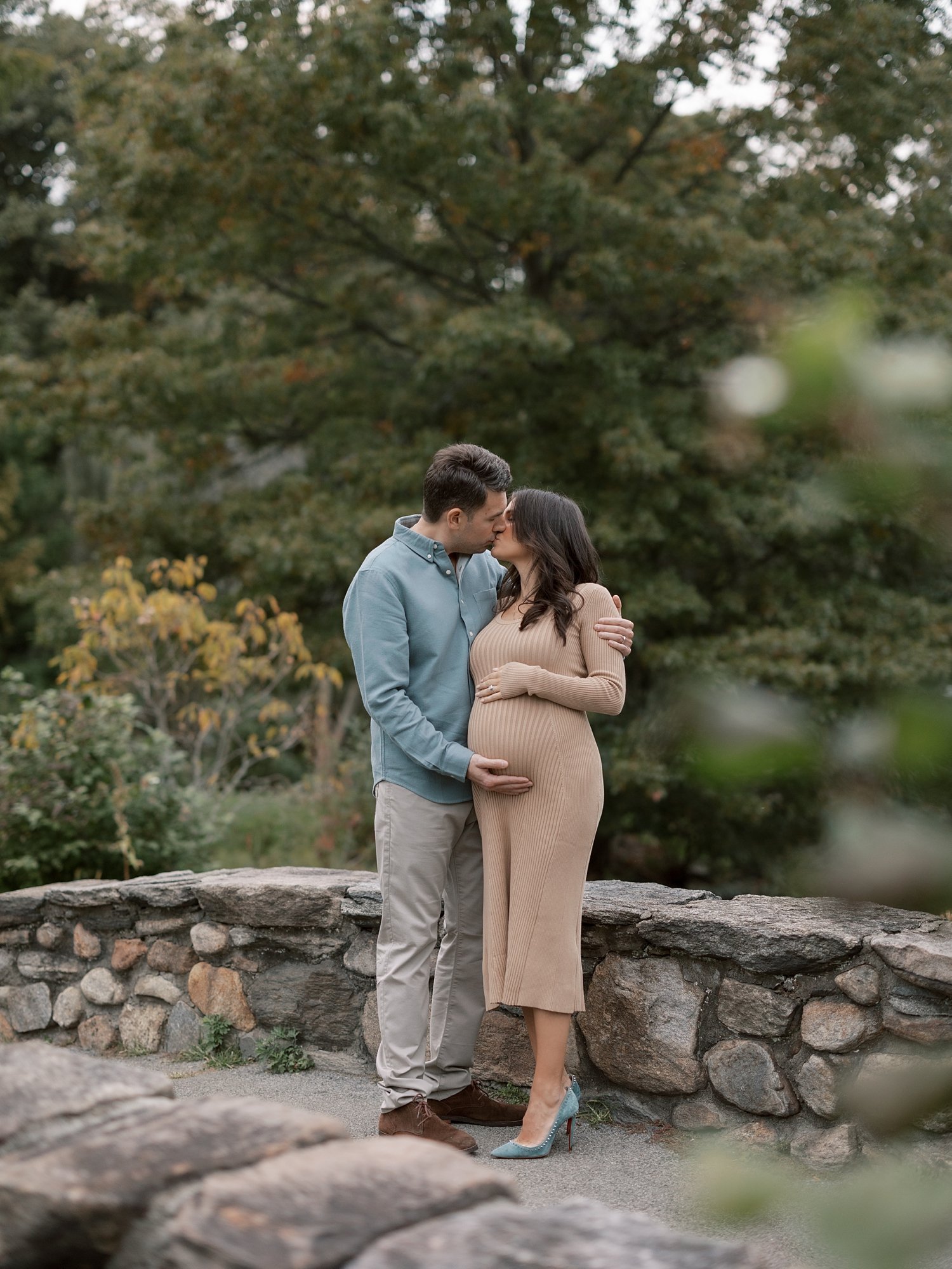 married couple kisses on stone bridge during fall maternity session in Binney Park