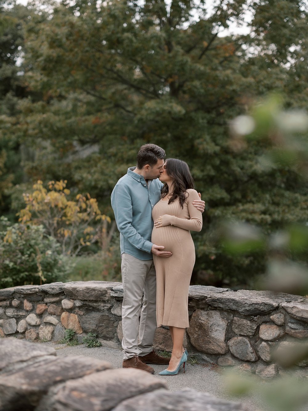 married couple kisses on stone bridge during fall maternity session in Binney Park