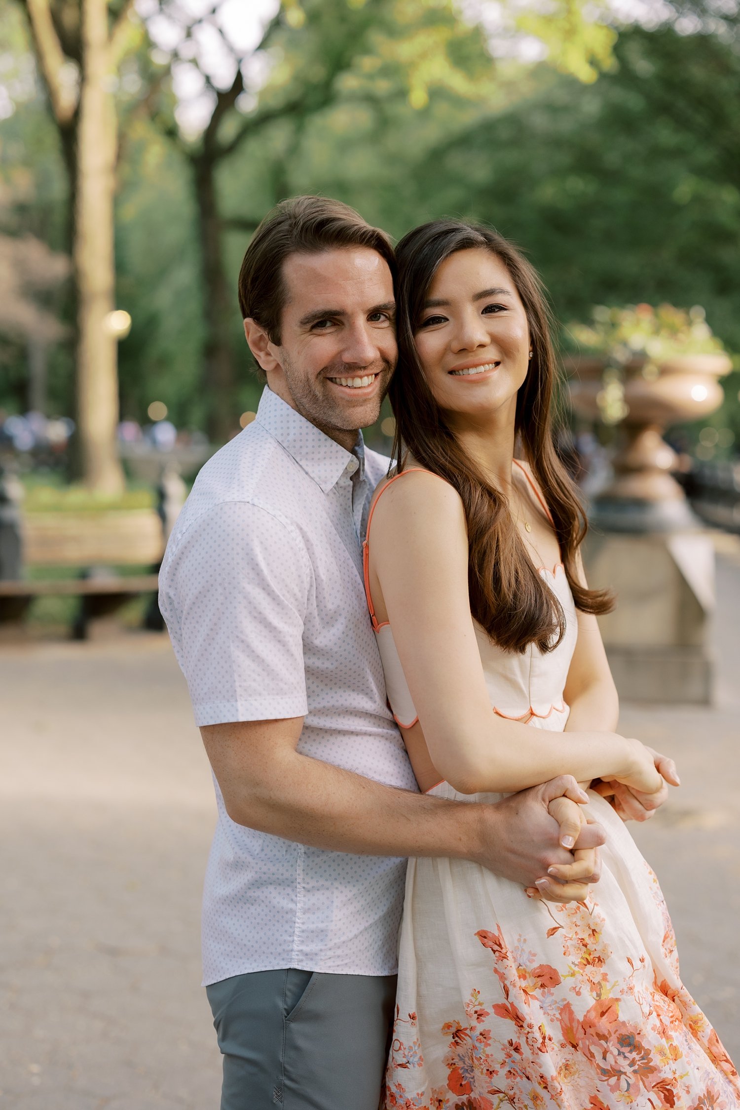 man hugs woman from behind during spring engagement portraits in Central Park