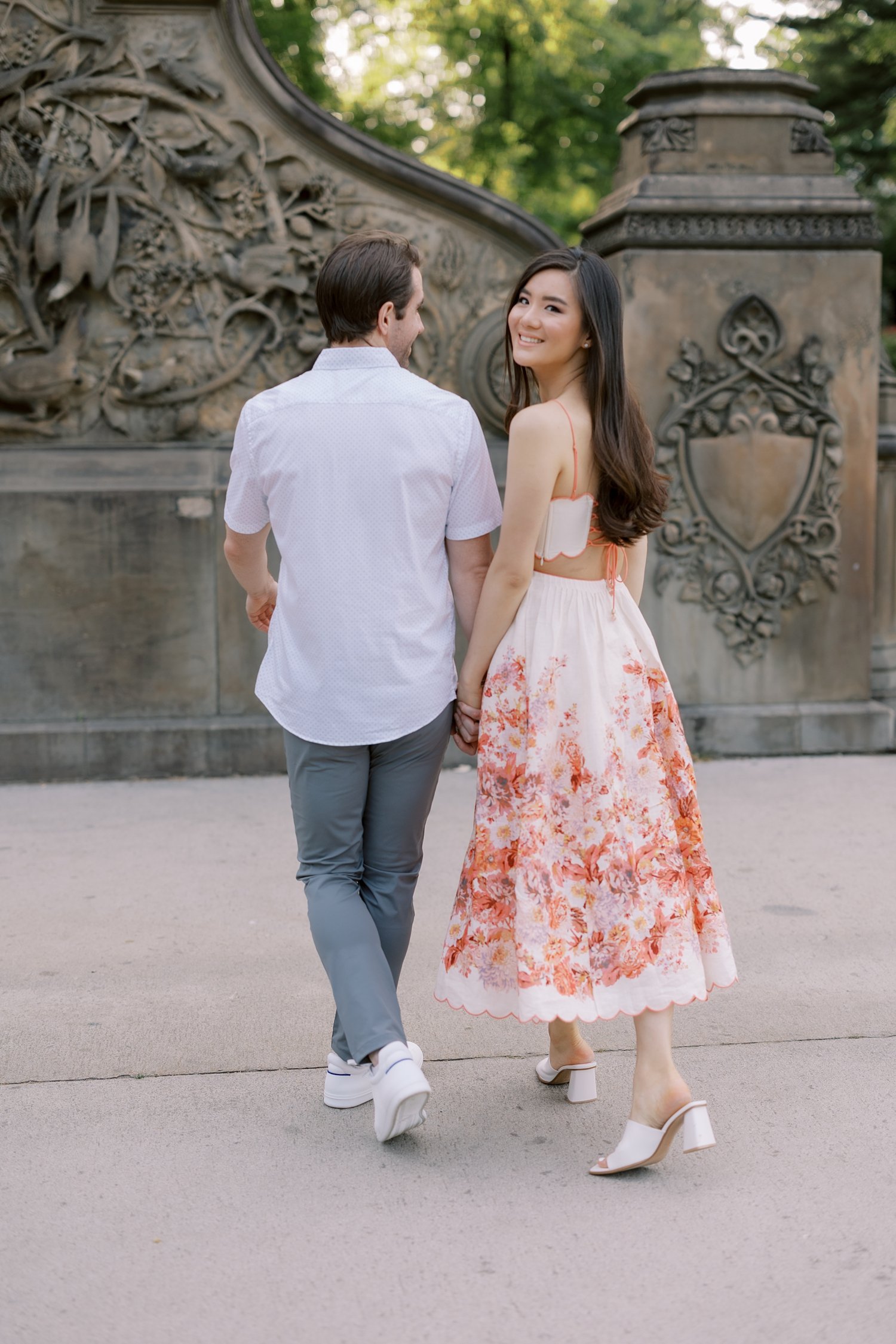 ended couple holds hands looking backwards during Central Park engagement portraits