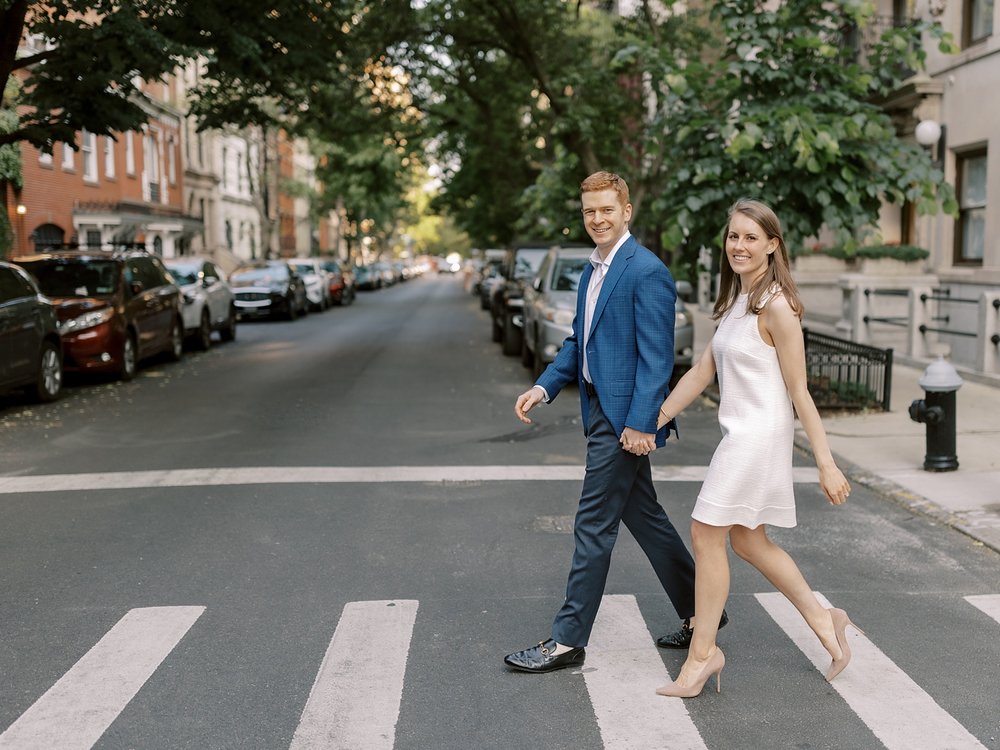 woman in white dress holds hands with man walking across crosswalk in NYC