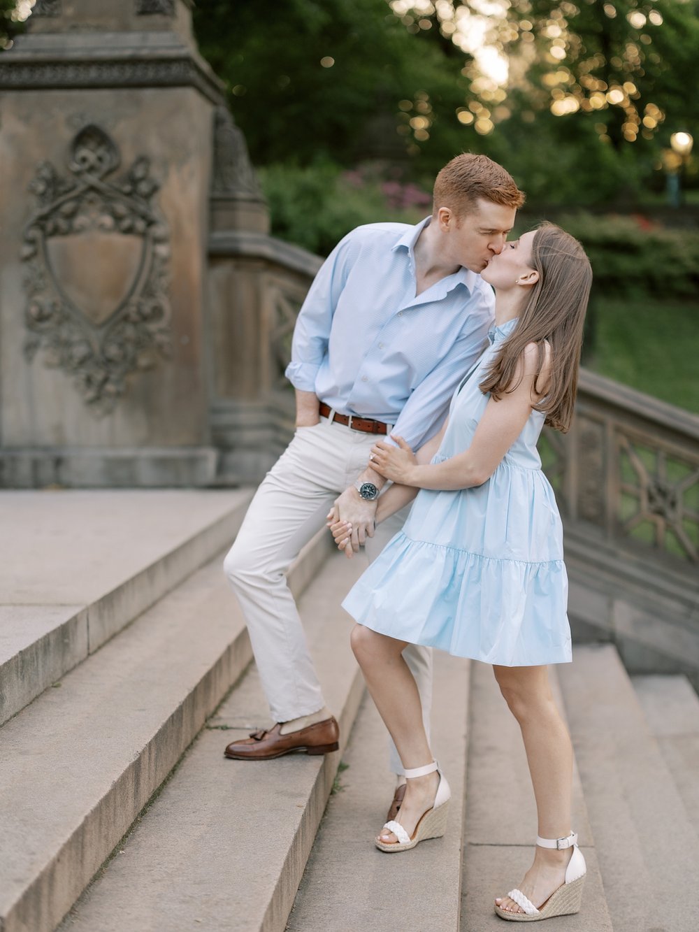 man leans down step to kiss woman standing on staircase inside Central Park