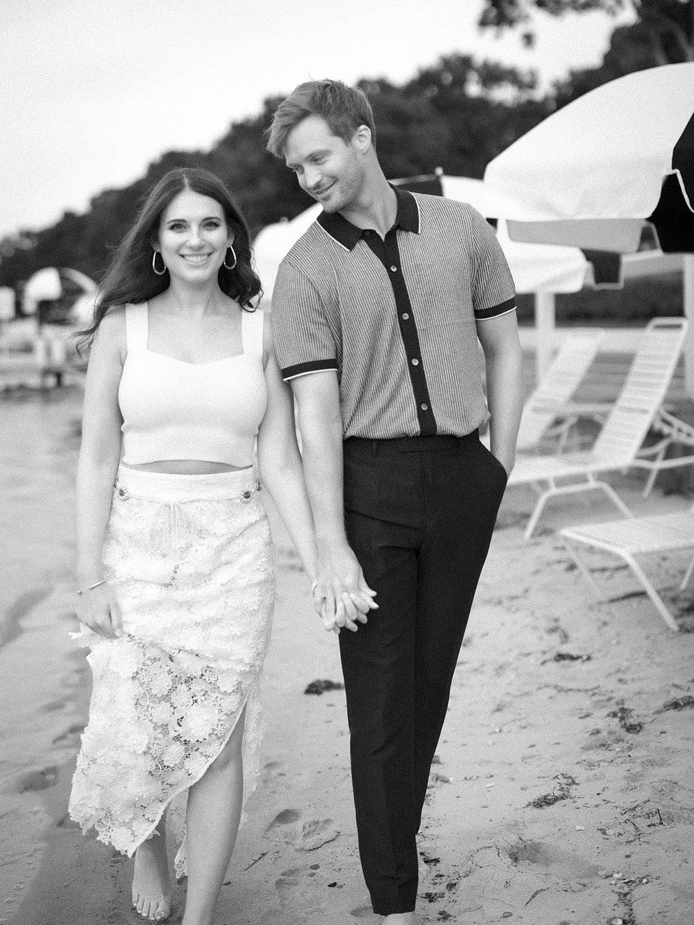couple holds hands on beach during engagement session at the Pridwin on Shelter Island NY