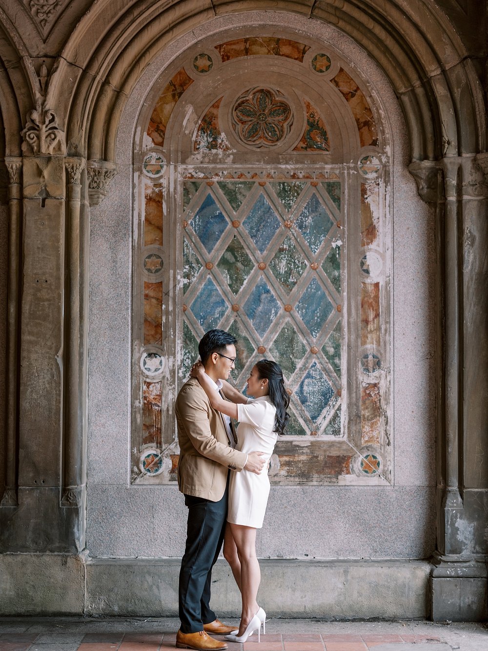 engaged couple hugs in front of mural under Bethesda Terrace in Central Park