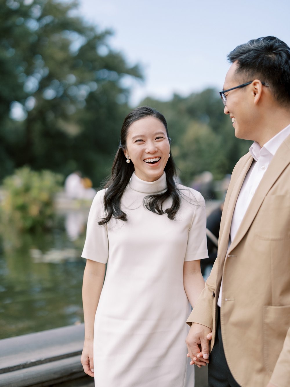 woman in white dress smiles at man while holding his hand in Central Park