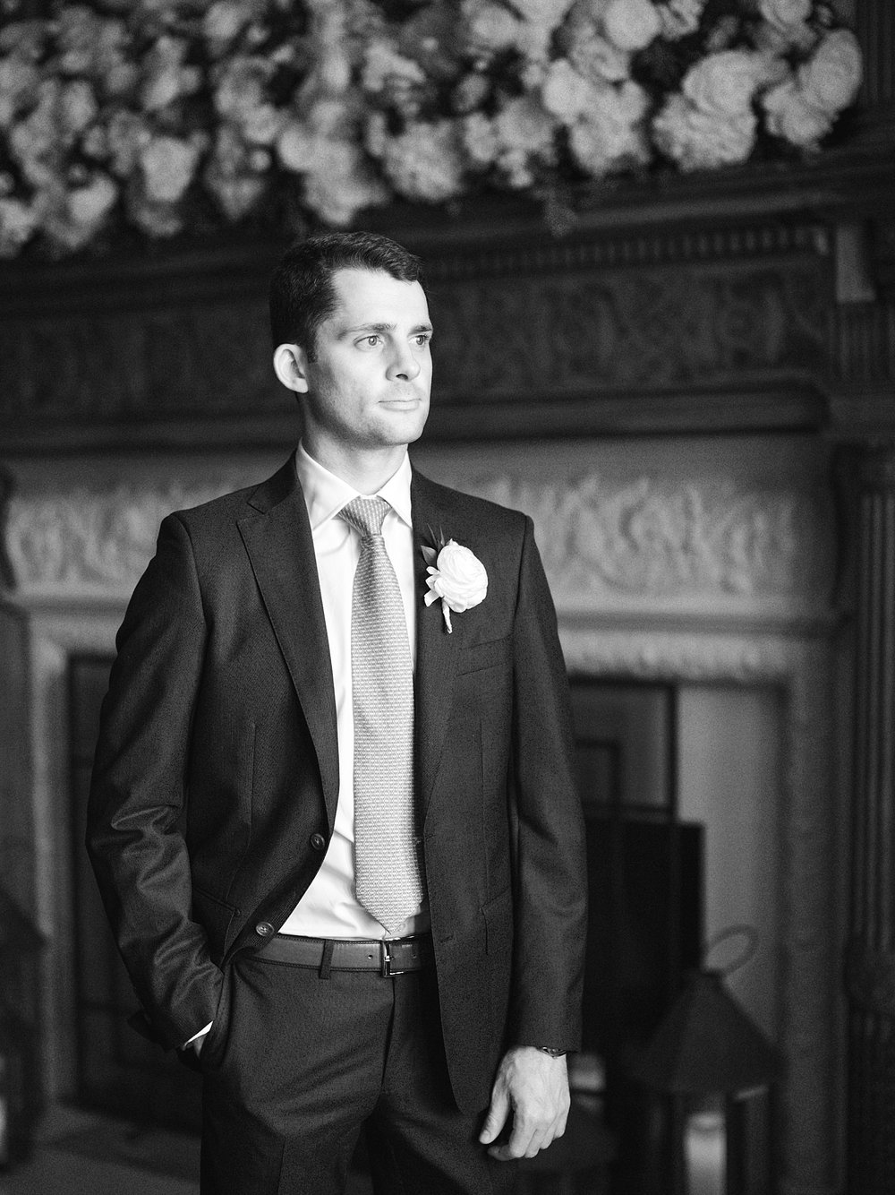 groom looks out window in front of fireplace inside the Mansion at Natirar