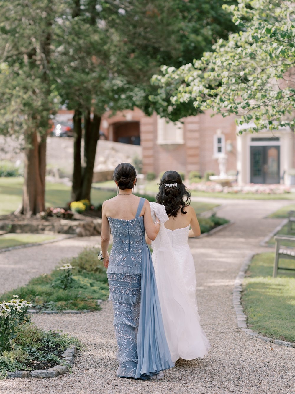 bride walks outside the Mansion at Natirar with mother holding dress
