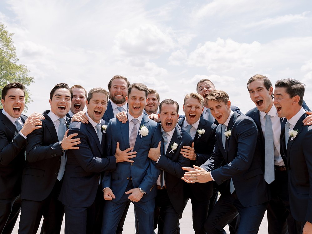 groom laughs with groomsmen in navy suits outside the Mansion at Natirar