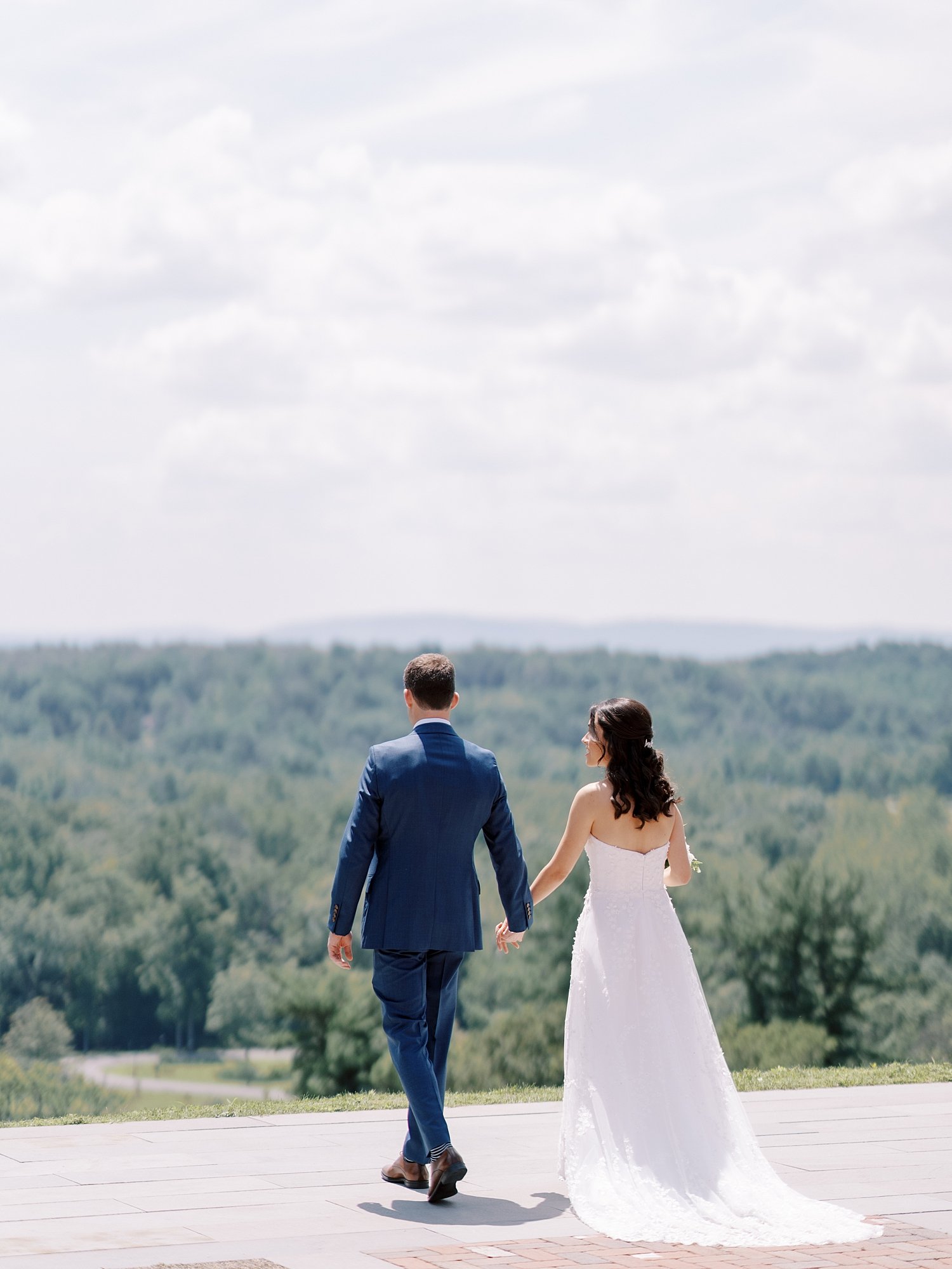 bride and groom hold hands walking towards hill outside the Mansion at Natirar