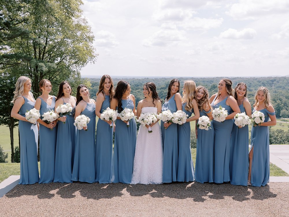 bride stands with bridesmaids in light blue dresses with white bouquets 