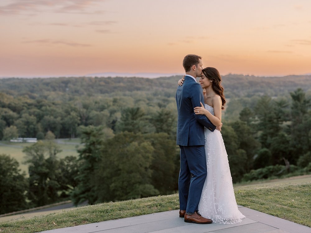 bride and groom hug on hill at sunset on the edge of Pendry Natirar