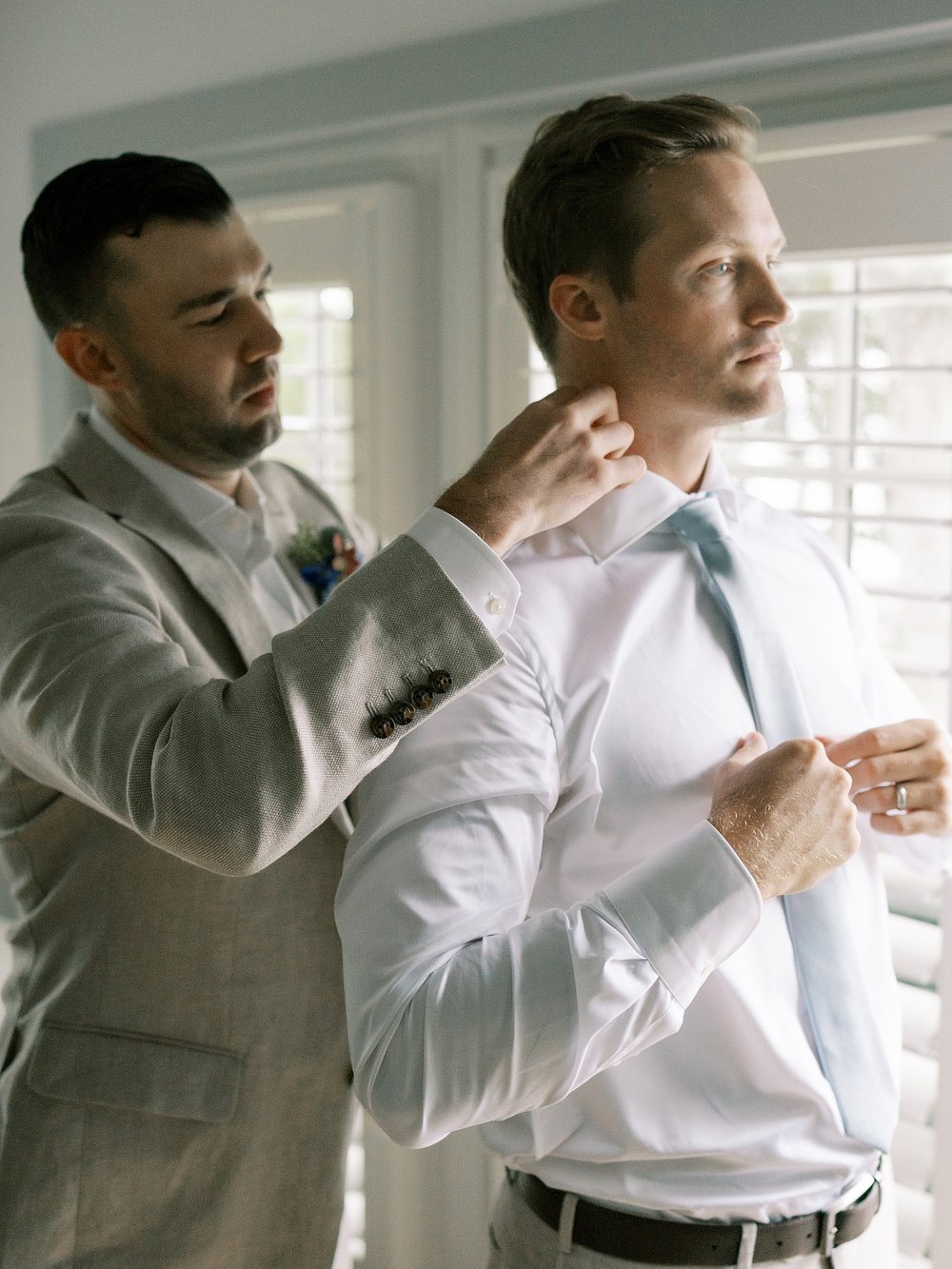 groomsman helps groom with blue tie before wedding at the Pridwin