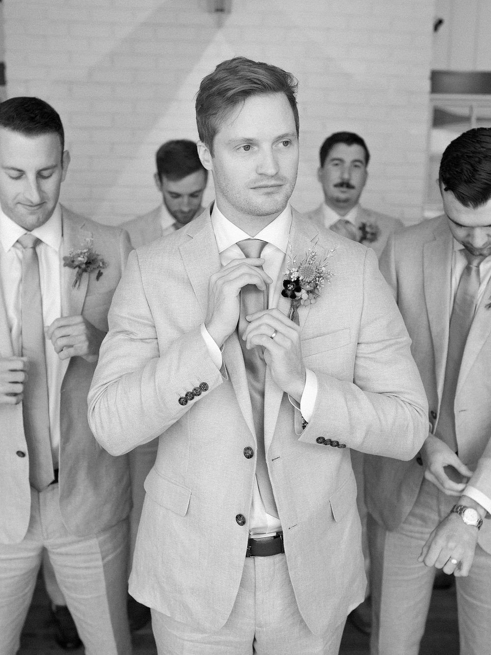 groom adjusts tie for linen suit 