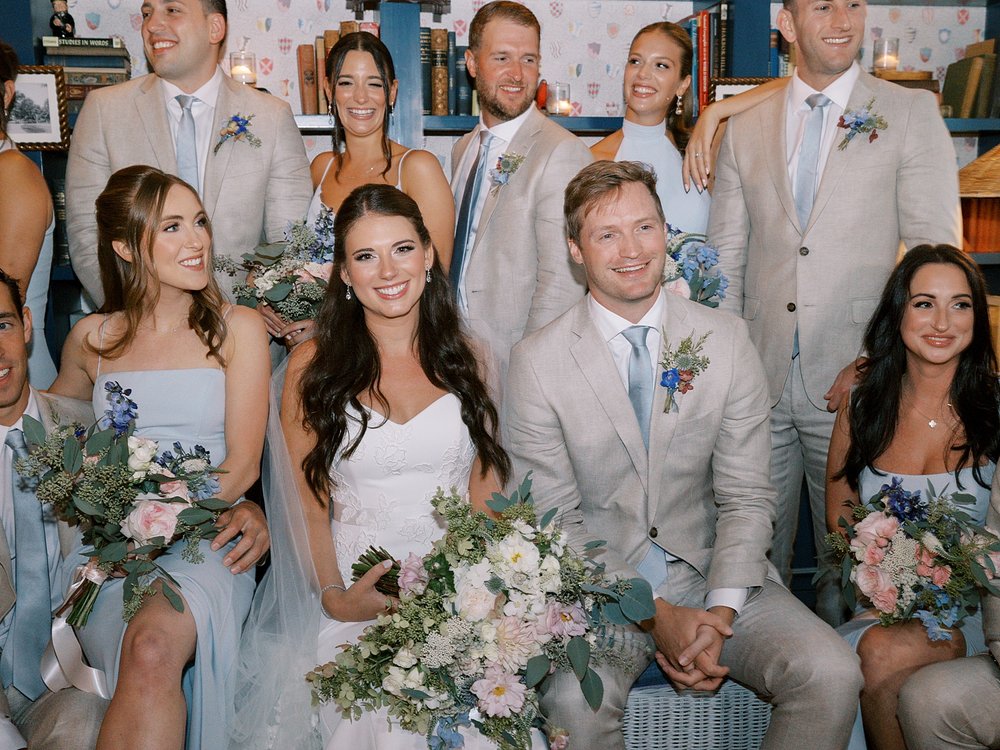 newlyweds sit surrounded by bridal party in tan and blue attire