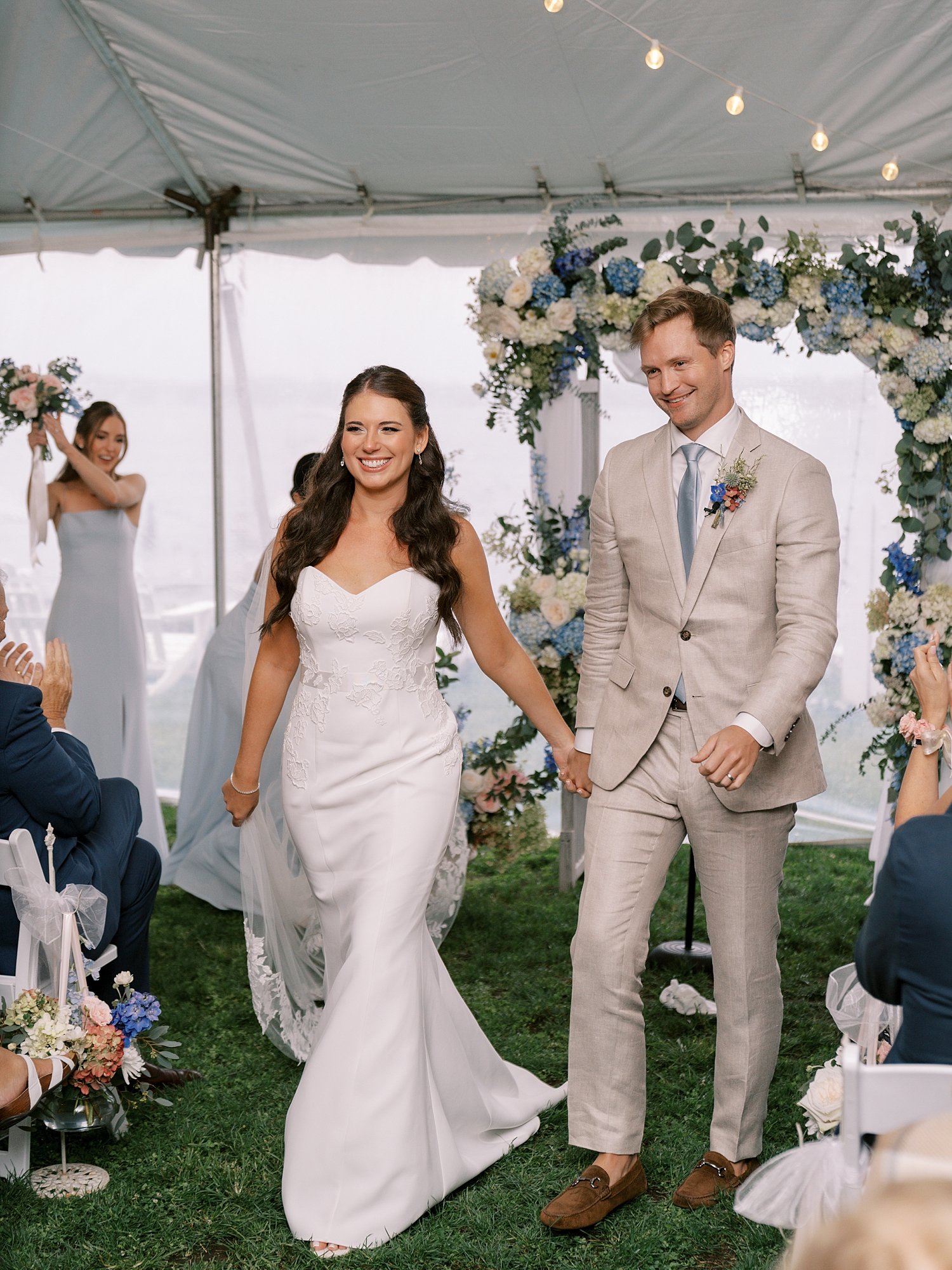 newlyweds hold hands leaving wedding ceremony under tent at the Pridwin