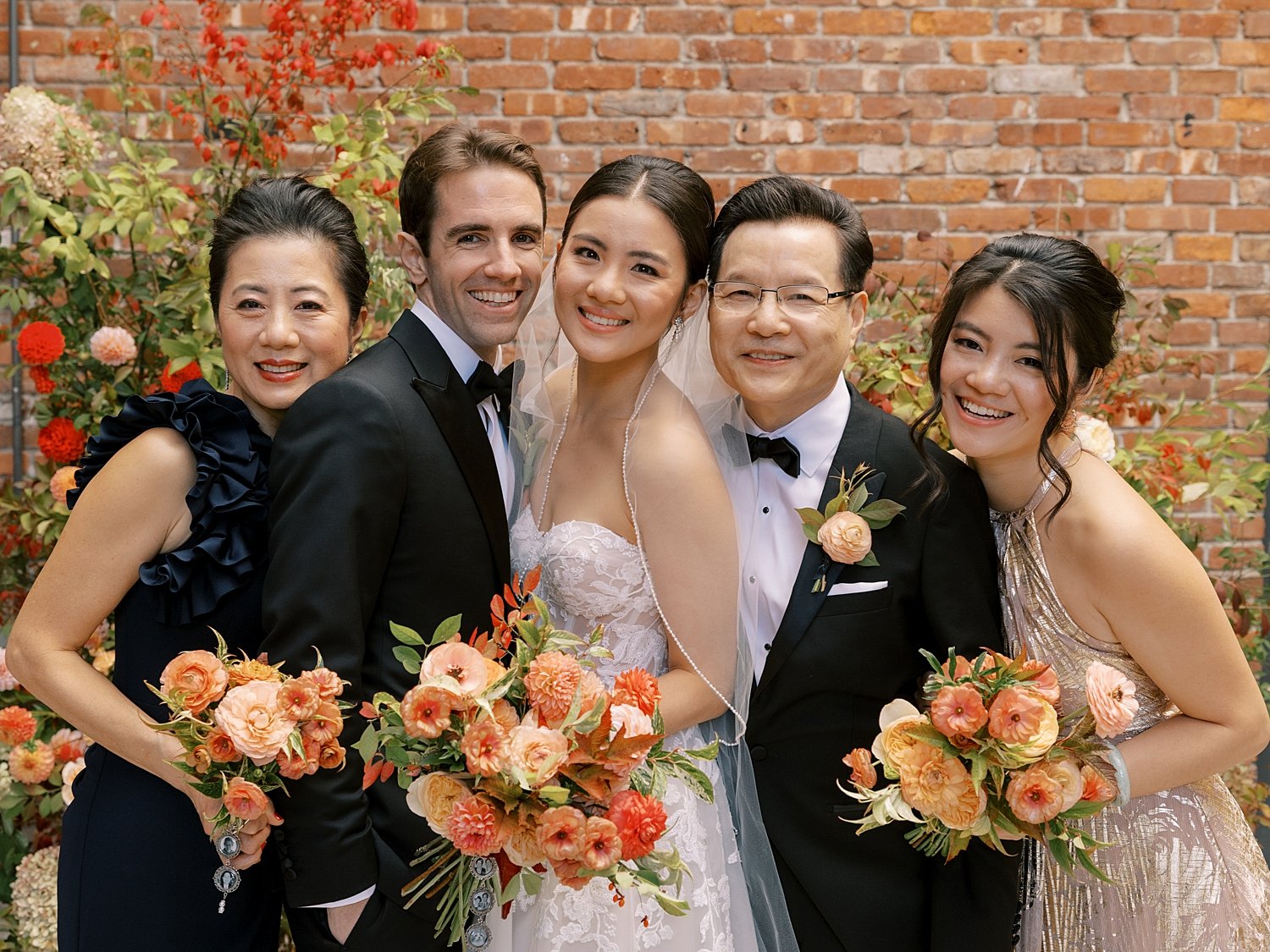 bride and groom pose with family in front of brick wall at the Wythe Hotel