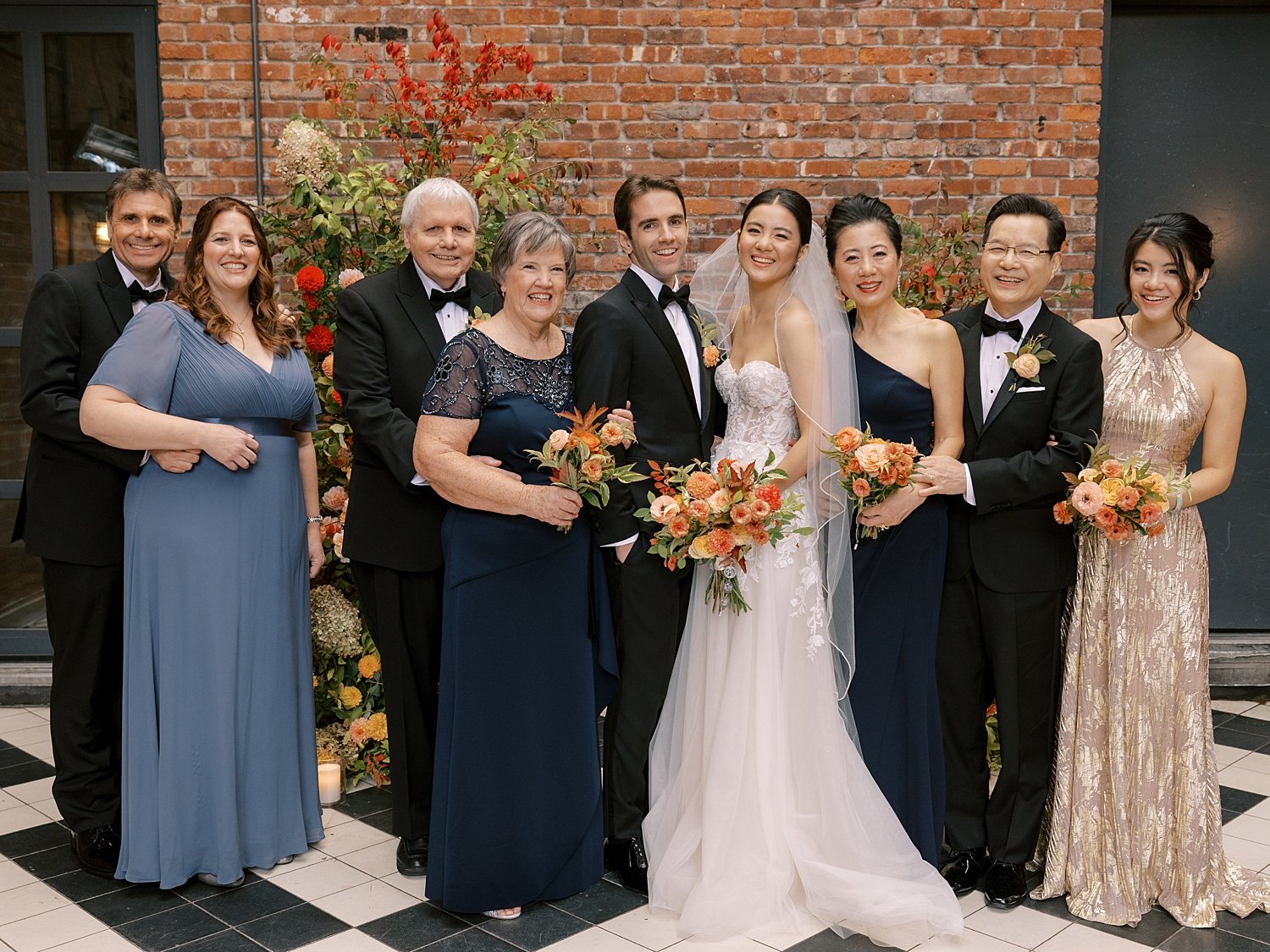 bride and groom pose with family in front of brick wall at the Wythe Hotel