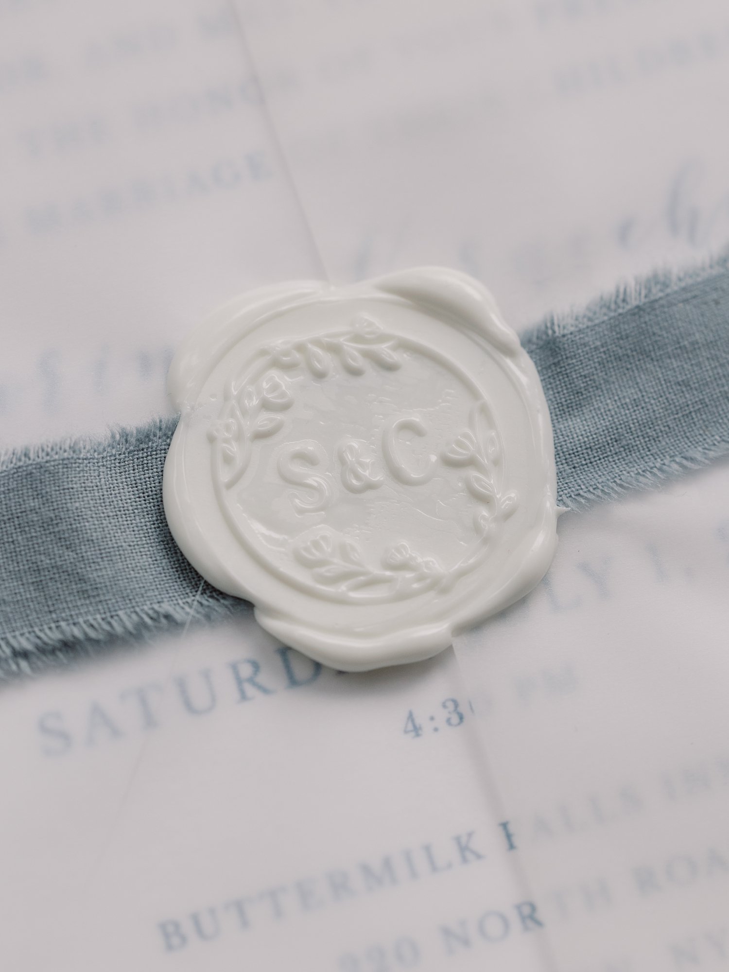 white wax seal with blue ribbon on invitation suite