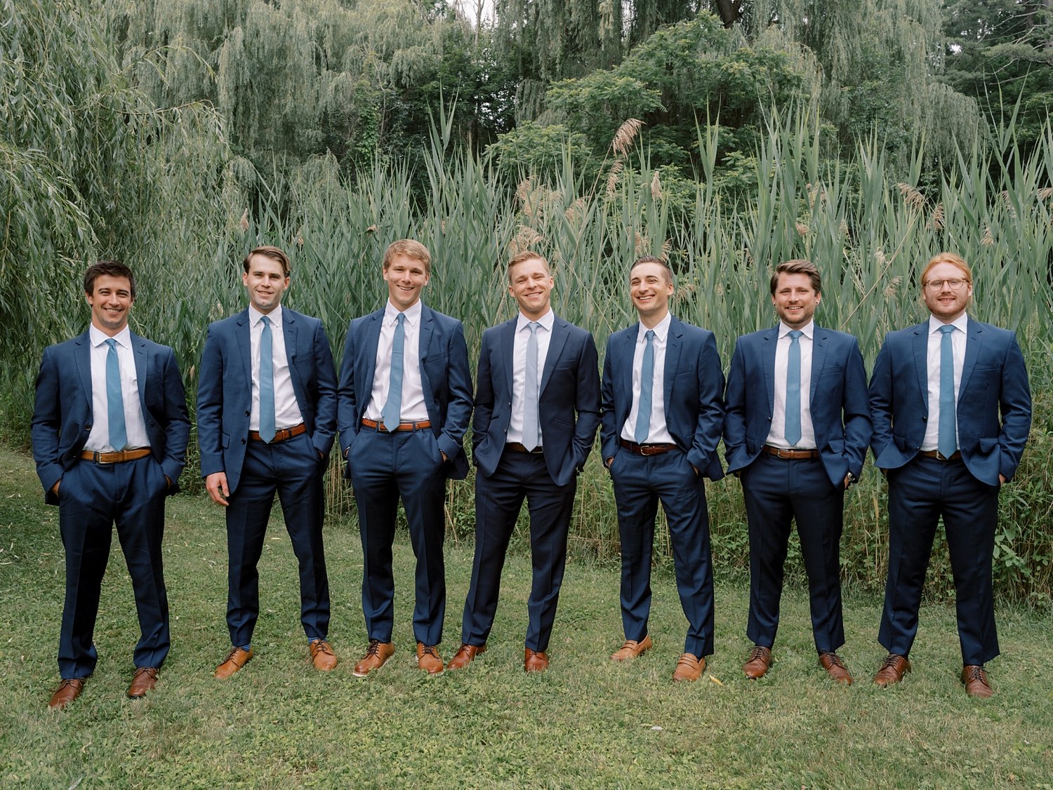 groom stands with groomsmen in navy suits with mint ties