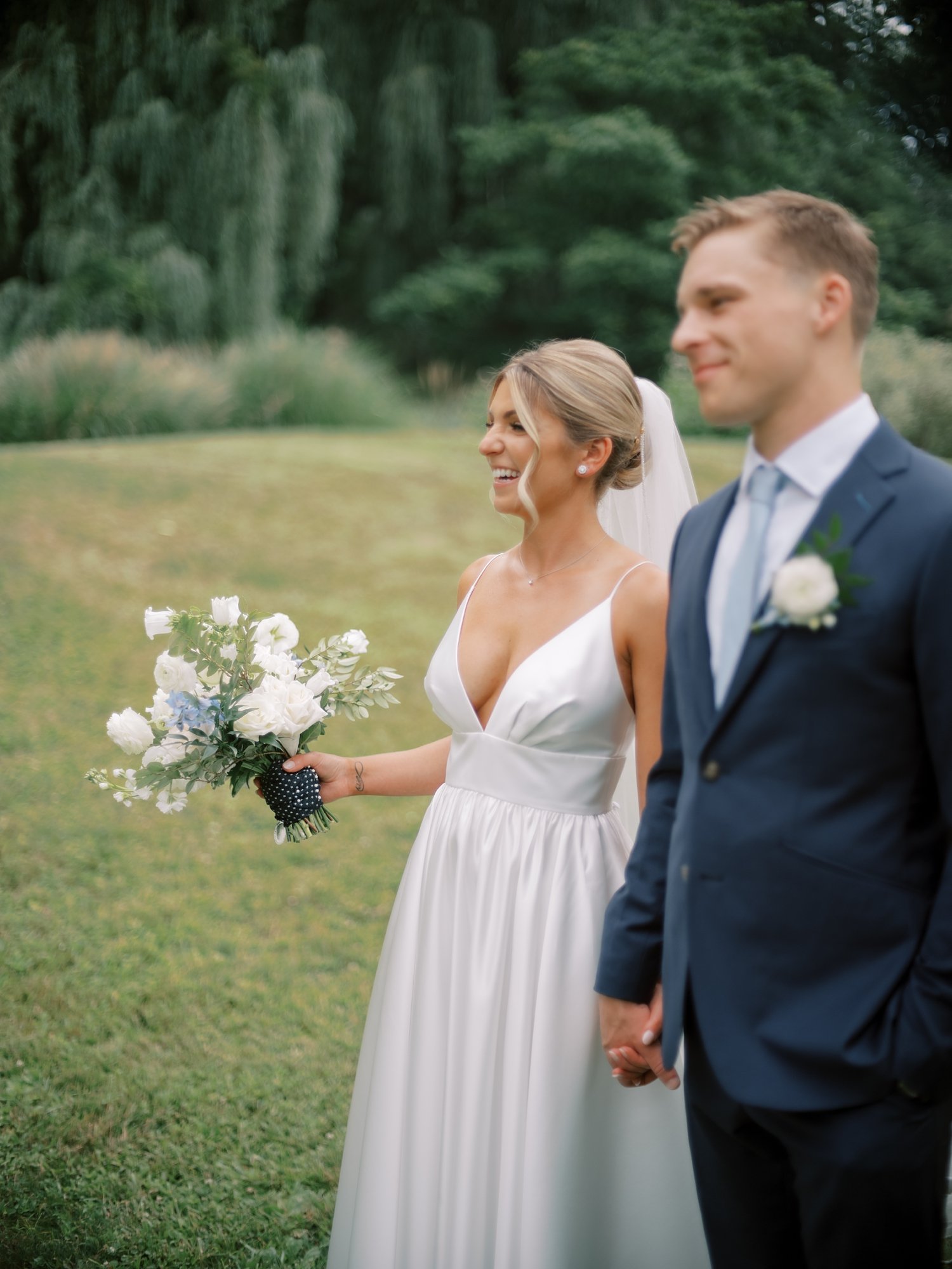 newlyweds hold hands walking near willow tree at the Buttermilk Inn &amp; Spa