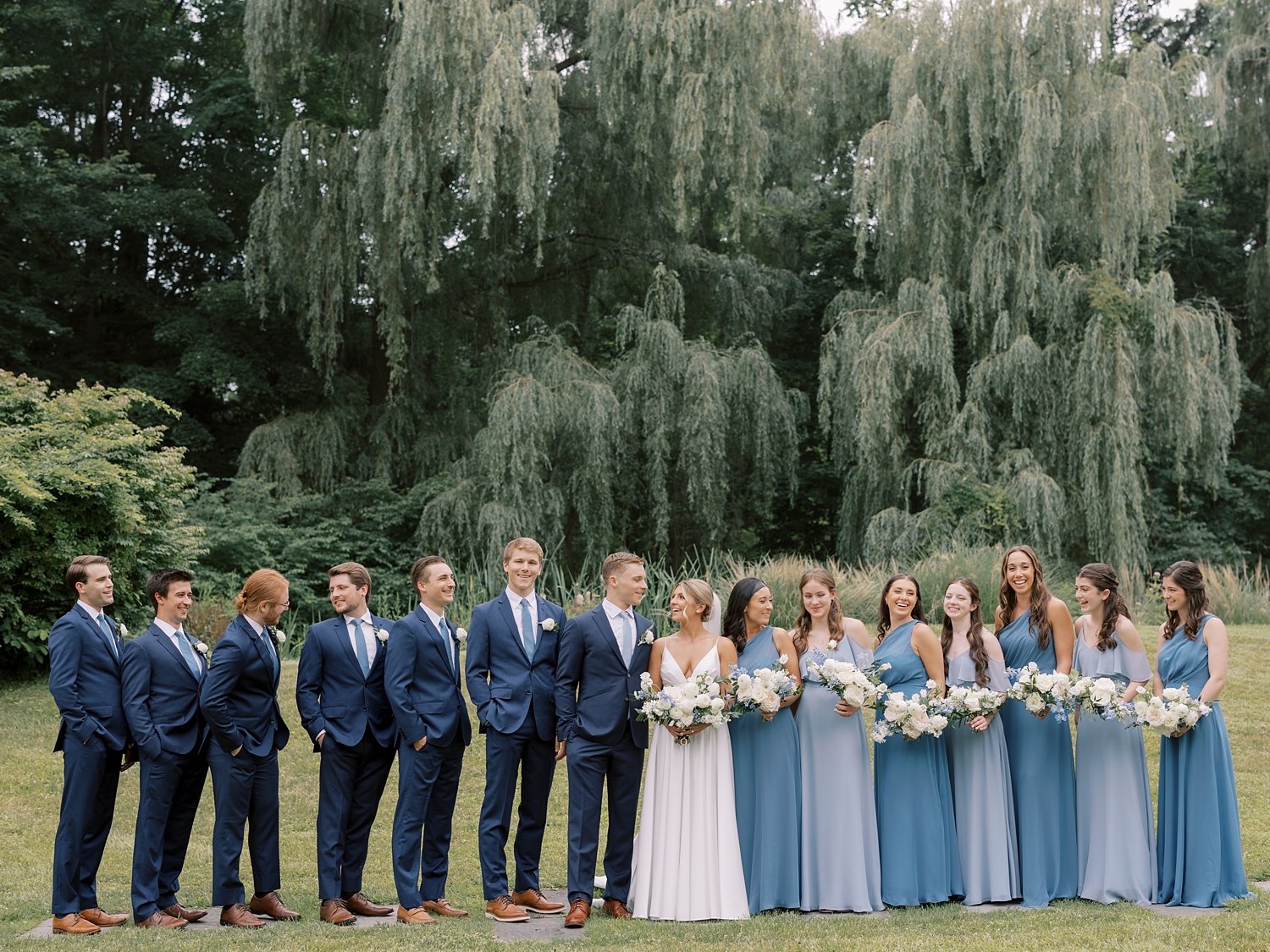 bride and groom pose with wedding party in navy blue suits and light blue gowns 