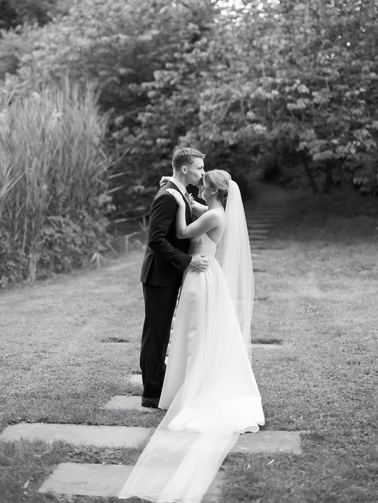 groom kisses bride's forehead on path at the Buttermilk Inn &amp; Spa