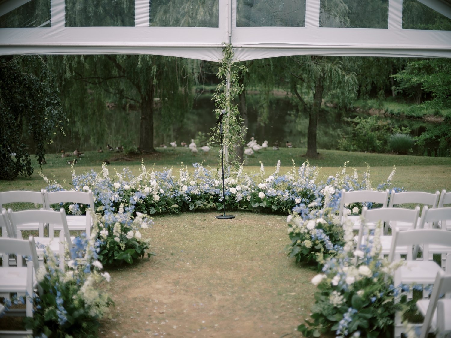 wedding ceremony under clear tent at the Buttermilk Inn &amp; Spa with blue and white flowers down aisle
