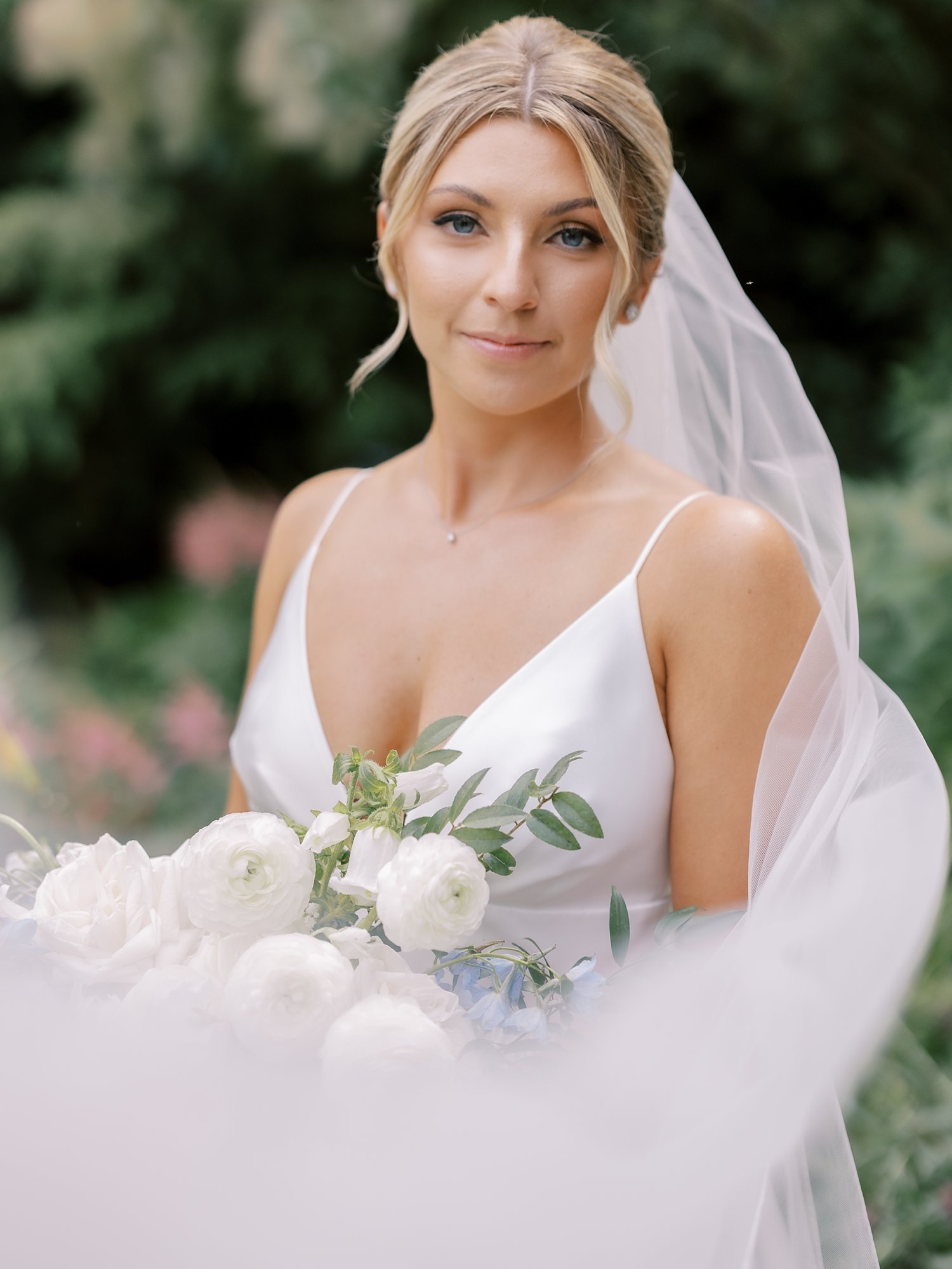 bride smiles with veil around her with white and blue flowers 