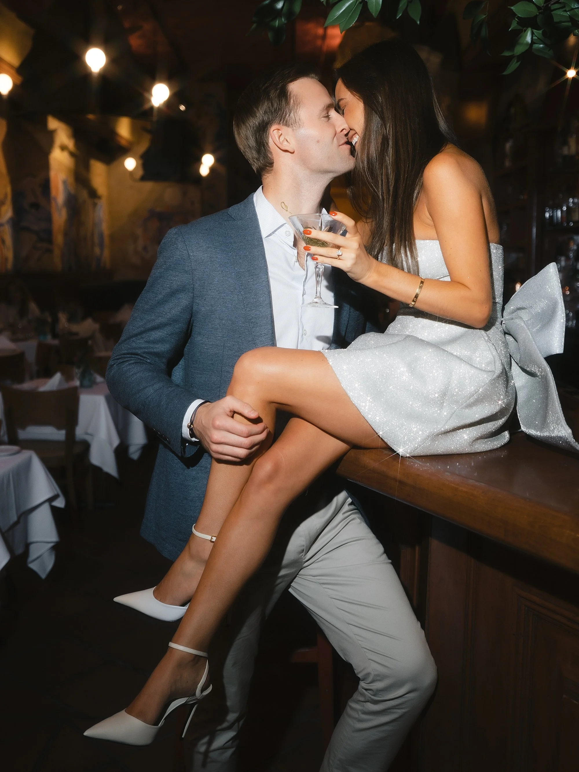 man reaches to kiss woman while she sits on bar inside Manhattan restaurant