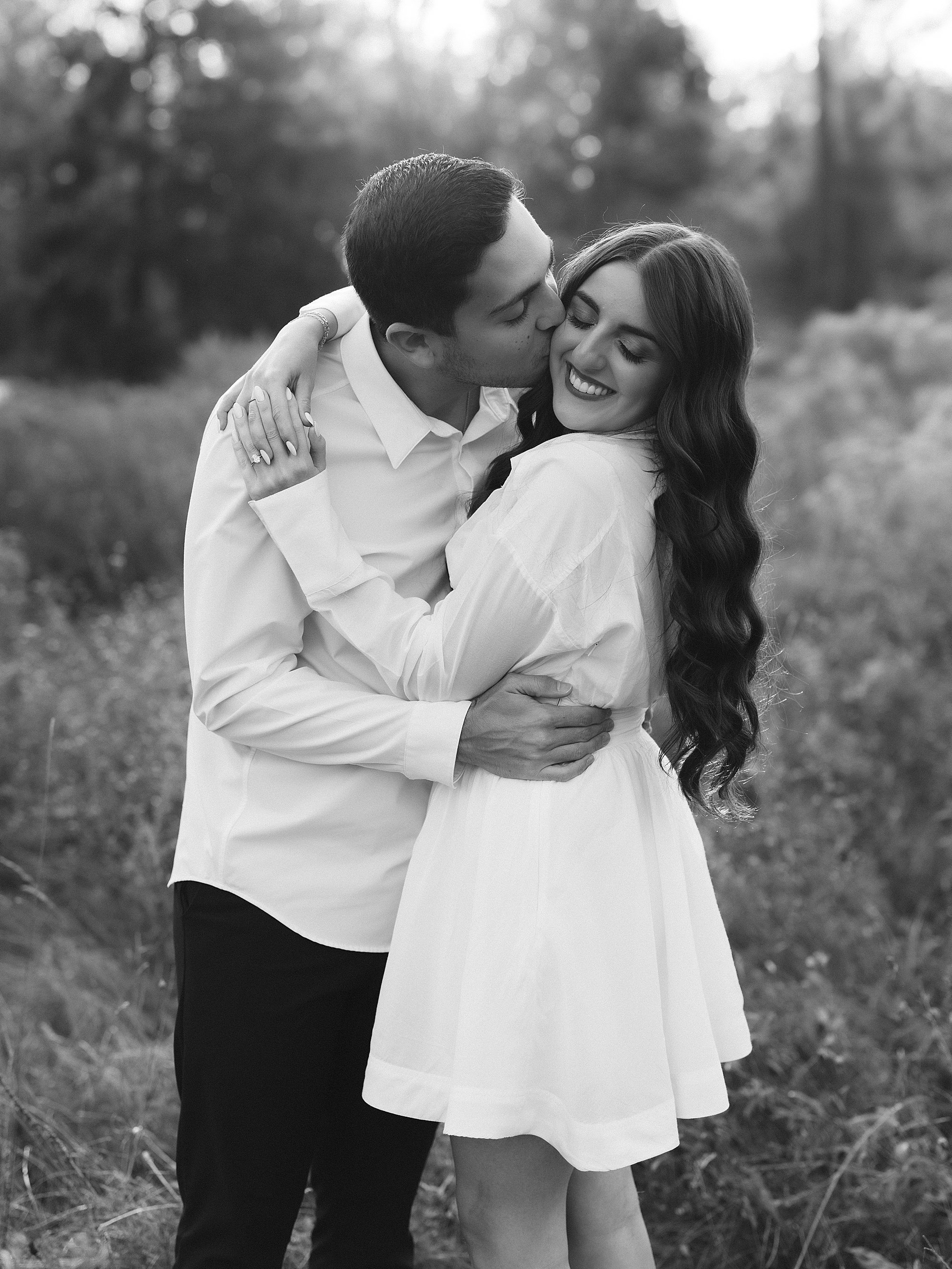 man hugs woman in short white dress during fall engagement photos at Testimonial Gateway Park