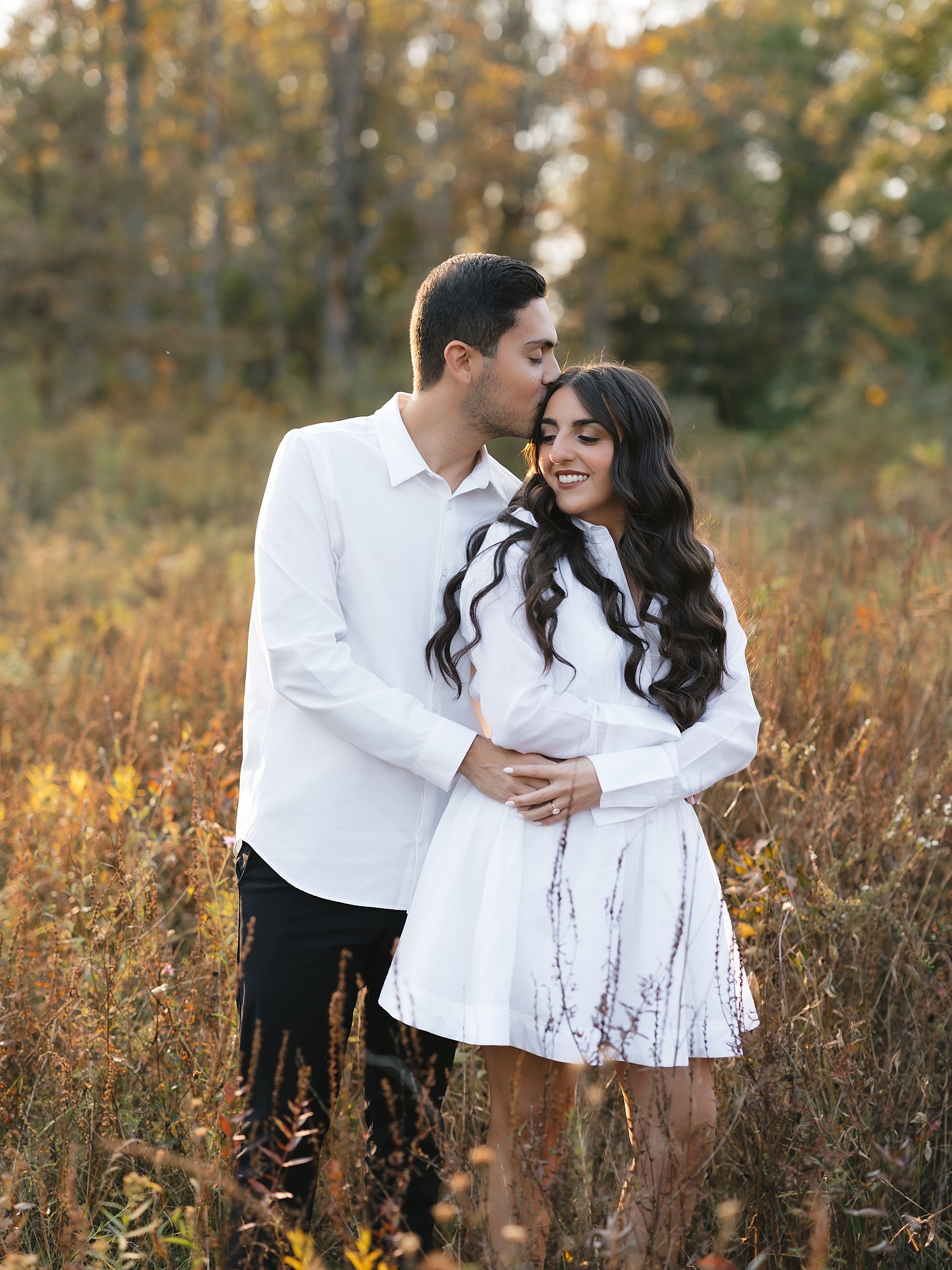 man hugs woman from behind during engagement session in field at Testimonial Gateway Park