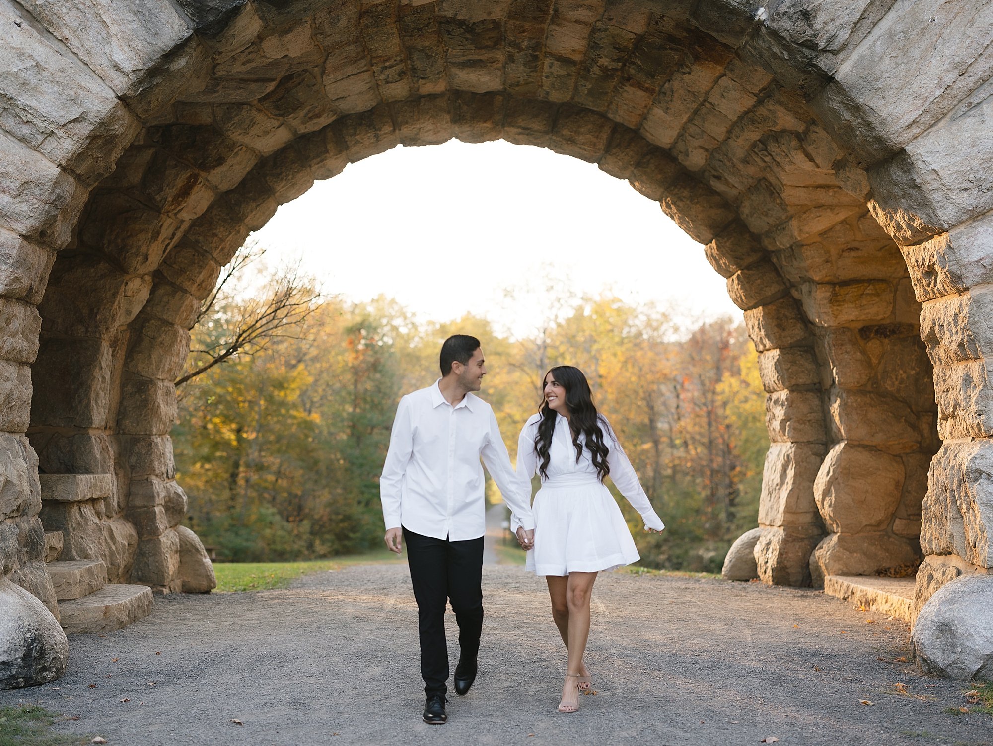 couple holds hands walking through stone archway at Testimonial Gateway Park