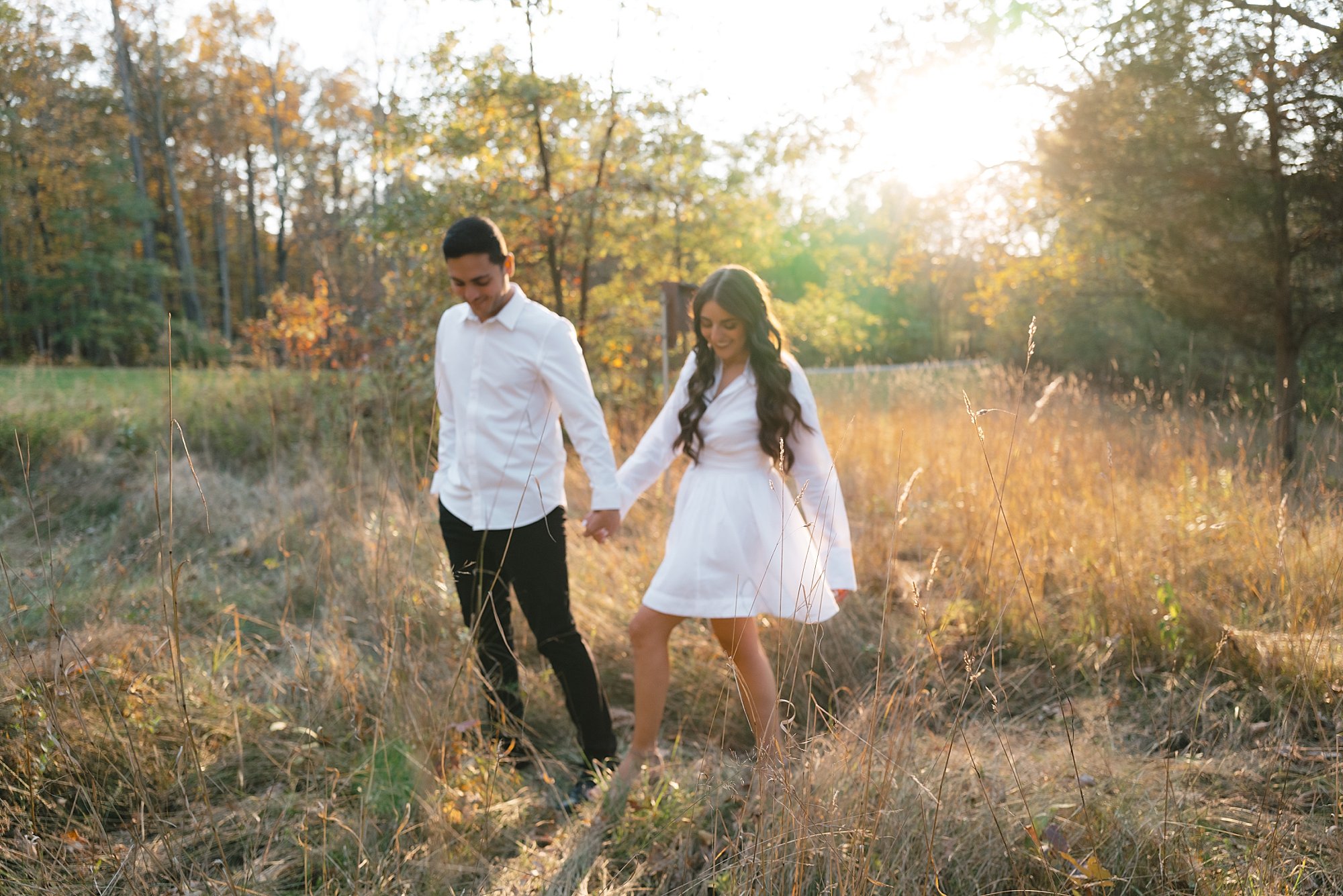 engaged couple holds hands walking through field at sunset at Testimonial Gateway Park